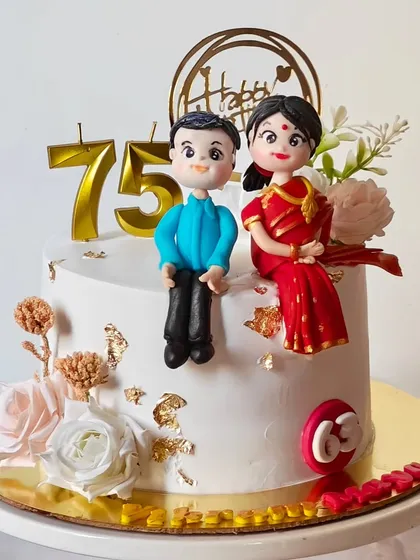A beautiful cake celebrating a 75th birthday, featuring handcrafted fondant figures of the couple in traditional attire. The cake is adorned with fresh flowers and gold leaf for an elegant finish.