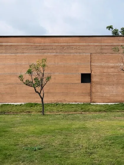 The monolithic rammed earth wall of the H.N. Science Center in Gauribidanur showcases the beauty of building with local soil. The horizontal layers tell the story of its construction, creating a facade that is both monumental and deeply connected to its site.