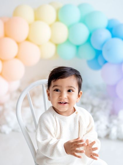 A happy baby boy clapping his hands during his rainbow-themed first birthday shoot.