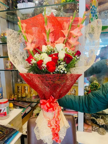 A large bouquet featuring red and white roses mixed with pink gladiolus flowers. The arrangement is wrapped in red and natural jute netting for a textured look.
