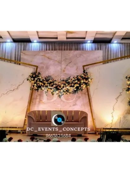 This modern wedding reception stage features a clean, elegant design with marble-finish backdrops, geometric gold frames, and asymmetrical floral arrangements for a sophisticated look.