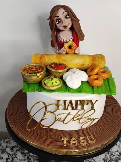A cake for a South Indian food lover! This design features a spread of delicious, handcrafted fondant treats, including a dosa, idlis, medu vadas, and bowls of sambar and chutney. The custom figurine on top makes it a truly personal and fun birthday surprise.