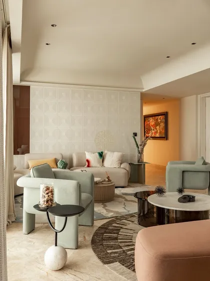 We used sculptural armchairs in a soft sage green to create an inviting conversation area. The layered rugs and mix of circular and organic shapes in the furniture add a playful, modern touch to this elegant living space.