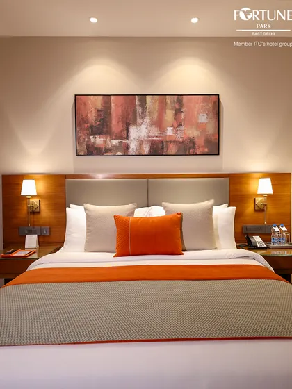 The bed is the centerpiece of our luxury room, with crisp white linens, plush pillows, and a striking orange runner for a pop of colour.
