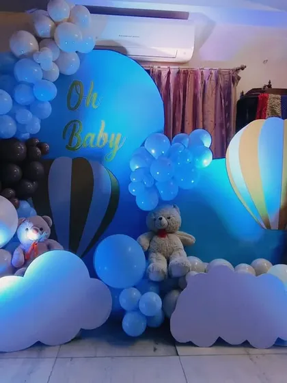 An "Oh Baby" shower with a hot air balloon theme. The setup uses blue and brown balloons to create a sky-like scene, complete with cloud cutouts, teddy bears, and 'BABY' blocks.