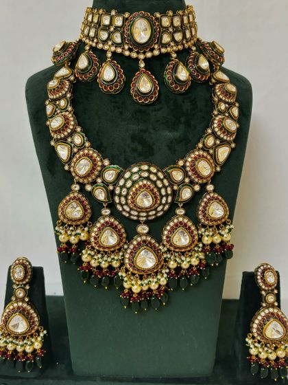 A heavy bridal necklace set available for rent, with a choker and a wide, cascading necklace. The design uses Kundan stones with red and green Meenakari details.
