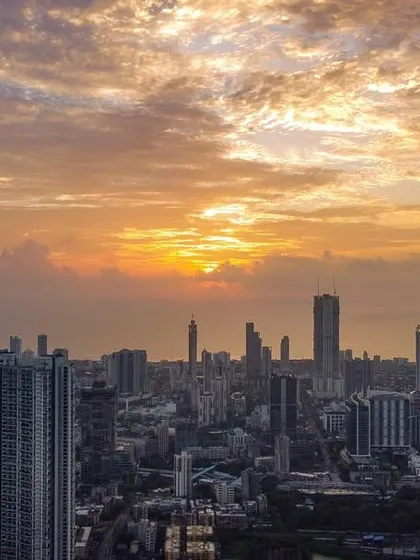 A wider view of a dramatic, cloud-filled sunset over the Mumbai cityscape, showing more of the urban landscape.