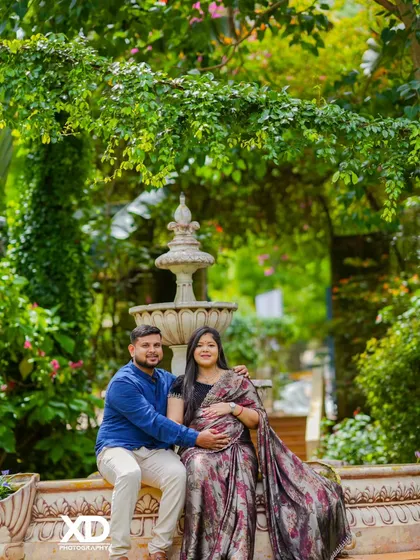 A classic couple's portrait in a garden, seated by a fountain, blending traditional wear with a romantic, natural backdrop.