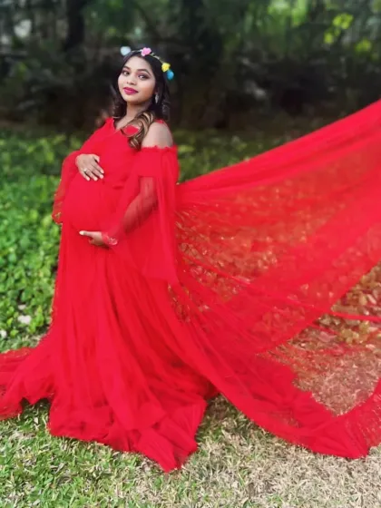 This vibrant red gown features a wide, ruffled trail and off-the-shoulder sleeves, offering a bold and glamorous look for an outdoor maternity shoot.