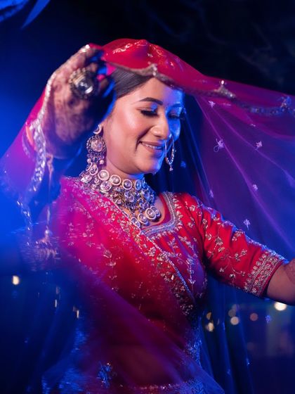 An artistic shot of a bride in a red lehenga, dancing with her dupatta. The blue lighting creates a dramatic and memorable image.