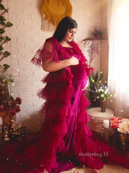 This mom-to-be is glowing in a deep red velvet and tulle gown. The soft lighting and romantic boho studio setup create a dreamy and enchanting atmosphere for her solo maternity portrait.