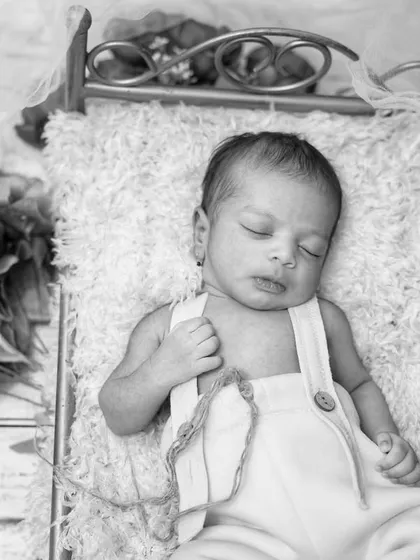 A timeless black and white portrait of a newborn sleeping on a miniature bed. This style emphasizes emotion and the delicate details of your baby.