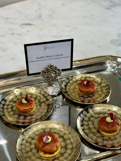 Awadhi Mutton Galouti, a melt-in-your-mouth kebab, served on small golden plates, reflecting the premium nature of the event.