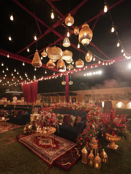 A cozy lounge setup at the Moroccan sangeet, complete with plush velvet sofas, layered rugs, and an overhead installation of Moroccan lamps. The space was surrounded by florals, making it feel like a luxurious oasis.