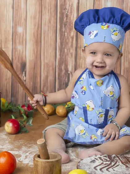 This little chef is having a great time playing with flour and a wooden spoon in his cute blue apron.