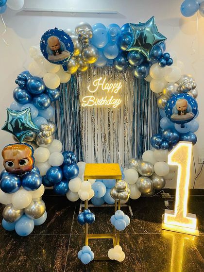 A "Boss Baby" theme for a first birthday. This cool setup features a blue and silver balloon ring, a shimmer curtain, a light-up '1', and Boss Baby character foil balloons.