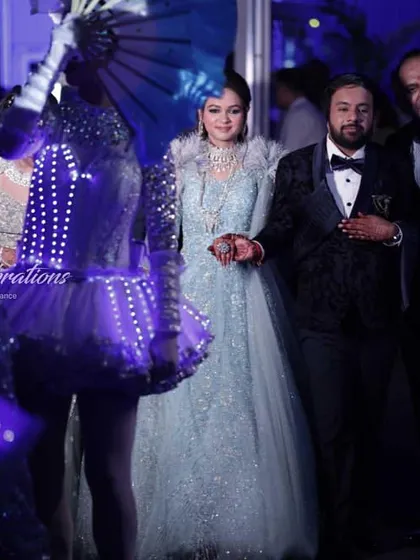 A close-up of the couple's sangeet entry, surrounded by dancers in illuminated LED costumes. The modern, glowing outfits provide a stunning contrast to the couple's elegant attire.