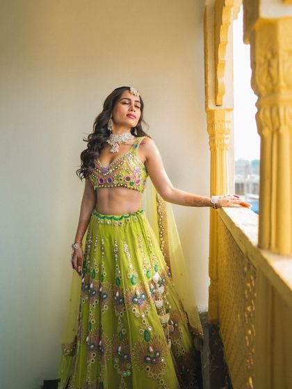 A stunning solo portrait of the bride in her vibrant green and yellow lehenga, basking in the sunlit glow of her Haldi day.