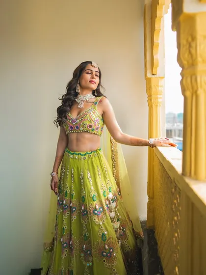 A stunning solo portrait of the bride in her vibrant green and yellow lehenga, basking in the sunlit glow of her Haldi day.