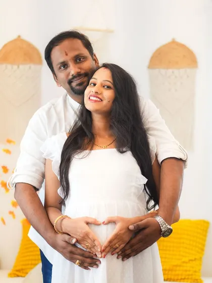 A classic couple pose for a maternity shoot, with both partners making a heart shape on the baby bump. It's a sweet and popular way to show their shared excitement.