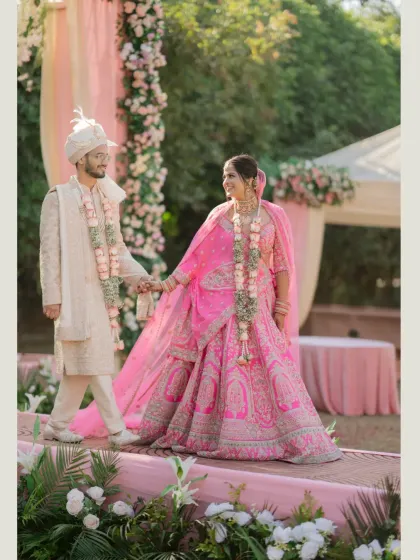 A beautiful, happy portrait of the couple walking hand-in-hand on their wedding day, dressed in vibrant pink and ivory.