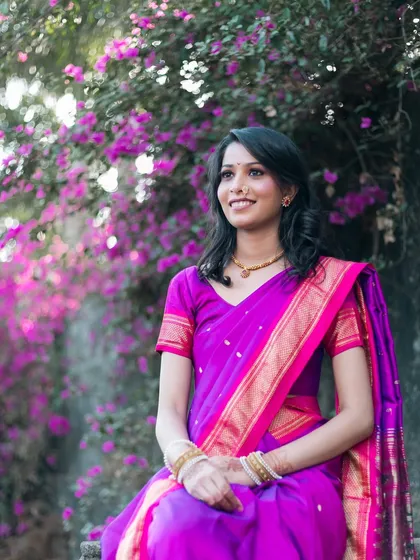 A bride in a vibrant purple saree, captured against a beautiful backdrop of pink bougainvillea flowers.