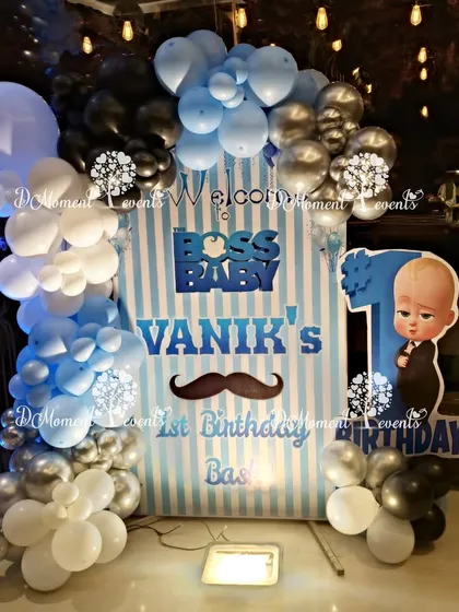 A welcome sign for "Boss Baby Vanik's 1st Birthday Bash," featuring a blue and white striped backdrop and a matching balloon garland.