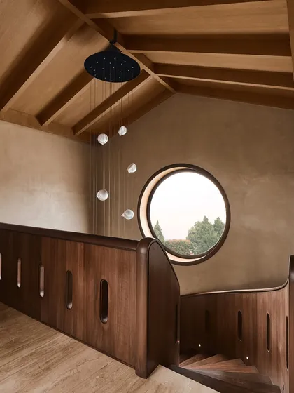 Looking down the spiral staircase from the upper level, this view shows the relationship between the wooden structure, the round window, and the pendant lighting, creating a harmonious architectural moment.