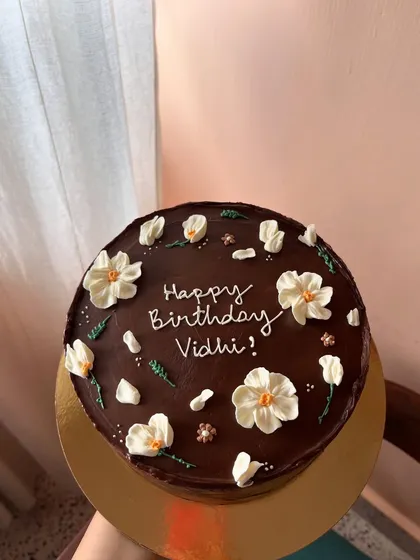 A rich chocolate ganache cake providing a beautiful dark canvas for delicate, hand-piped white buttercream flowers.