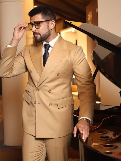 A guest strikes a pose by the piano, his hand adjusting his glasses. This image captures the suave, intellectual aesthetic that a well-made bespoke suit can convey.