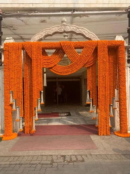 For a more traditional ceremony, I created this beautiful entrance using drapes of bright orange marigolds. The addition of white floral tassels adds a touch of elegance to this classic and auspicious decoration.