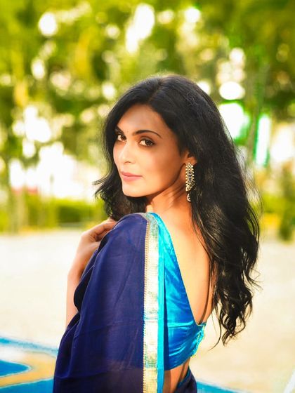 A classic over-the-shoulder pose in a blue saree. This outdoor shot highlights her elegant profile and the beautiful drape of the fabric.