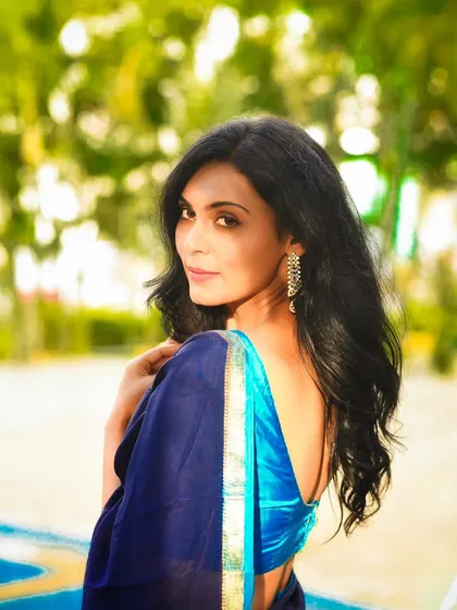 A classic over-the-shoulder pose in a blue saree. This outdoor shot highlights her elegant profile and the beautiful drape of the fabric.