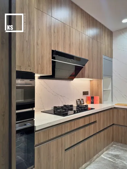 This L-shaped kitchen layout features integrated ovens and a hob, all surrounded by durable wood-laminate cabinetry. The design ensures a smooth workflow between cooking and prep areas.