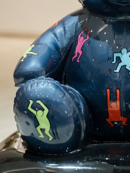 Another detail of the Keith Haring teddy, focusing on the dynamic poses of the colorful figures on its arm and knee.