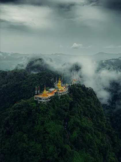 The famous Tiger Cave Temple perched on a mountain in Krabi, surrounded by clouds. A challenging climb with a rewarding, spiritual view.