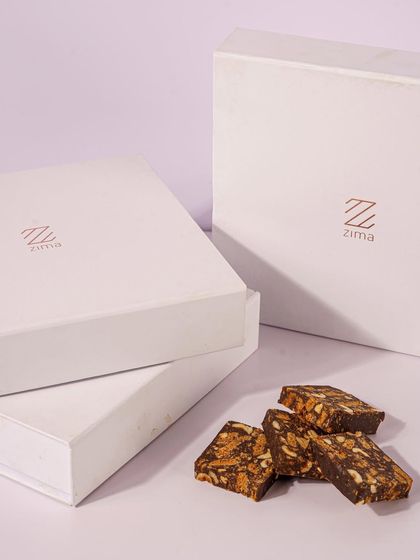 A minimalist product shot focusing on the elegant branding of Zima's dessert boxes and a sample of the chocolate bark. This type of image is great for building brand identity and for use on a clean, modern website.