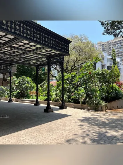 The black metal pavilion provides a shaded area for drop-off and arrival. Its intricate design contrasts with the soft, organic forms of the surrounding garden.