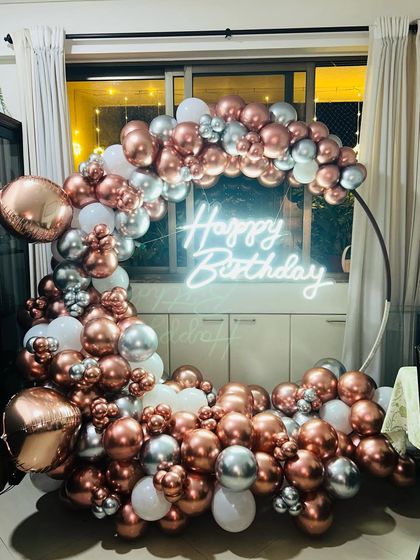 A beautiful rose gold, silver, and white balloon semi-arch for a birthday celebration at home. The neon sign adds a warm glow to this elegant setup.
