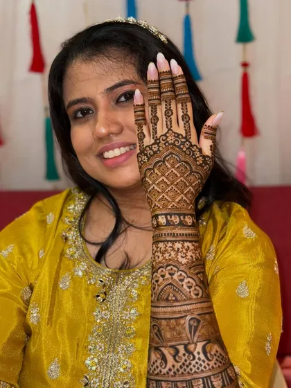 A smiling bride holding up her hand to show the detailed grid pattern on her bridal mehendi.
