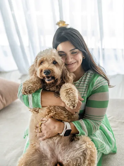 A beautiful portrait celebrating dog-moms. A woman in a green striped dress lovingly holds her fluffy cockapoo, both sharing a moment of pure connection.