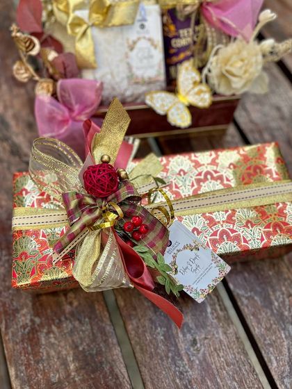 A close-up of a beautifully wrapped gift in red and gold paper, topped with an intricate bow and a custom tag. This is traditional festive gifting, elevated with a refined and polished finish.