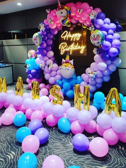 A magical unicorn-themed birthday party decoration. This setup includes a circular balloon arch in shades of pink, purple, and blue, unicorn foil balloons, and the birthday girl's name in foil letters.