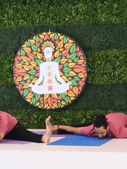 A moment of contrast and connection during a partner yoga demonstration. One person rests while the other achieves a deep forward fold, showing the balance of effort and ease in the practice.