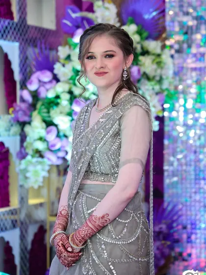 A full-length view against a festive background. The makeup and hair are perfectly suited for a glamorous wedding reception.