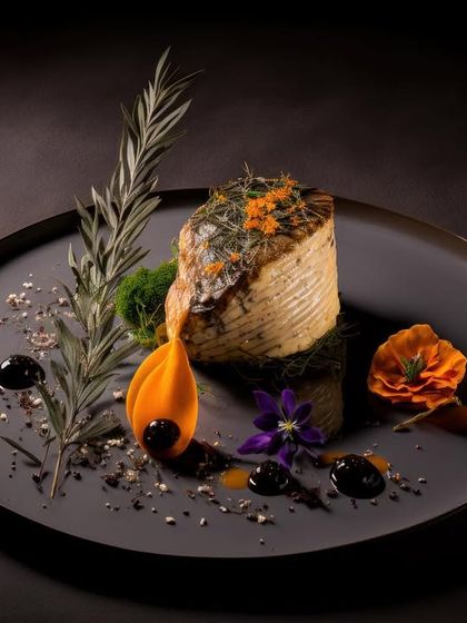 A culinary composition of Smoked Salmon layered with pumpkin leaves. The dish is artfully decorated with rosemary, edible flowers, and drops of balsamic reduction, demonstrating a sophisticated approach to flavour and aesthetics.