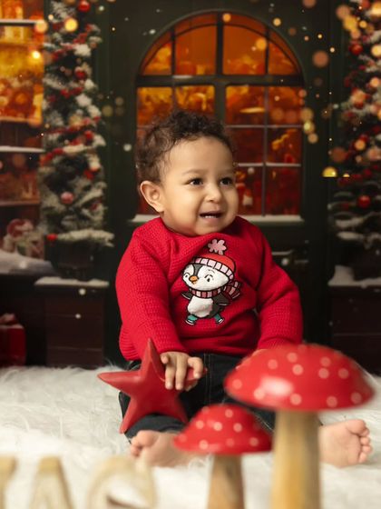 A candid moment of a baby boy in a Christmas sweater, looking delighted by the festive props.