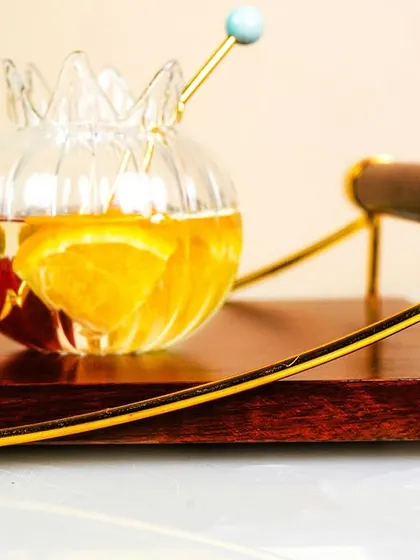 A close-up of a unique glass and serving tray, showcasing a fruit-infused drink. The details of the glassware and the rich wood of the tray are the focus here.