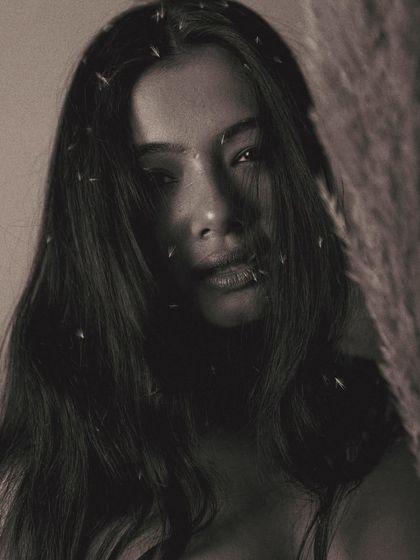 A hauntingly beautiful portrait where the model's face is partially obscured by shadow and the prop. The specks of light in her hair add a touch of magic to the dark, grainy image.