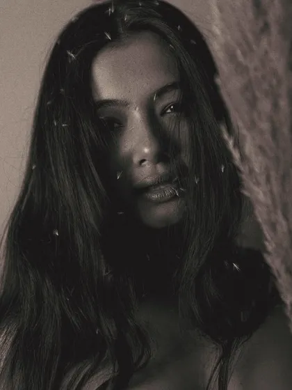A hauntingly beautiful portrait where the model's face is partially obscured by shadow and the prop. The specks of light in her hair add a touch of magic to the dark, grainy image.